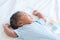 Portrait of African Nigerian newborn baby sleeping with raise hands and toy is beside on white bed at home. Innocence infant with