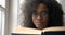 Portrait Afro American beautiful pretty wearing glasses reading book window home 4k leisure close up.