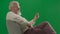Portrait of aged bearded man on chroma key green screen background. Full shot of senior man sitting on a chair holding