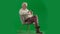 Portrait of aged bearded man on chroma key green screen background. Full shot of senior man sitting on a chair holding