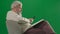 Portrait of aged bearded man on chroma key green screen background. Full shot of senior man sitting on chair reading