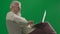 Portrait of aged bearded man on chroma key green screen background. Full shot of senior man sitting on a chair working