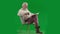 Portrait of aged bearded man on chroma key green screen. Full shot senior man sitting on chair reading book and drinking