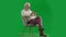 Portrait of aged bearded man on chroma key green screen. Full shot senior man sitting on chair surfing web on smartphone