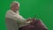 Portrait of aged bearded man on chroma key green screen. Senior man in casual clothing sitting on chair holding