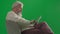 Portrait of aged bearded man on chroma key green screen. Senior man in casual clothing sitting on chair and using tablet
