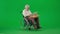 Portrait of aged disabled man on chroma key green screen. Senior man sitting in wheelchair with laptop on the pillow