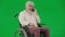 Portrait of aged disabled man on chroma key green screen. Senior man sitting in wheelchair and talking on smartphone.