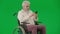 Portrait of aged man on chroma key green screen. Senior man in wheelchair typing bank card number in smartphone, buying