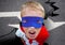 Portrait of aggressive super boy in red cape and blue mask on road