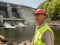 Portrait of an aging worker in a helmet against the backdrop of hydroelectric turbines