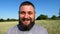 Portrait of agronomist with beard against background of green wheat. Happy smiling farmer looks into camera standing at