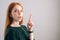 Portrait of amazed redhead young woman model pointing up with finger, looking at camera on white background.