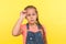 Portrait of amazed stylish little girl in denim overalls taking off pink eyeglasses and looking with astonished expression