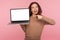 Portrait of amazed woman pointing at laptop with white screen copy space, mock up display for internet advertising