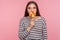 Portrait of amazed woman in striped sweatshirt licking lollipop, tasting sweet round rainbow candy with surprised expression