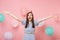 Portrait of amazed young happy woman in birthday hat blue dress screming spreading hands on pastel pink background with