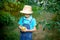 Portrait of an angry boy six years old in blue clothes and hat in a garden with Apple trees and holding apples