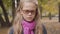 Portrait of an angry Caucasian teenage girl standing in the autumn park and looking at the camera. Young schoolgirl in