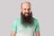 Portrait of angry crazy middle aged bald man with long beard in light green t-shirt standing with mad face, clenching teeth and