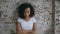 Portrait of angry curly mixed race woman looking into camera nervous on brick wall background