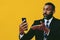 portrait of angry expressive bearded man in suit and tie with smartphone video call pointing hand at camera yellow