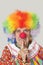 Portrait of angry senior male clown with finger on chin over light gray background