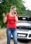 Portrait of angry young woman talking by phone and calling assistance to her broken car in field