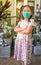 Portrait of Asian child girl wearing protective face mask, standing in front of plant shop, cross arm on chest, eyes looking at