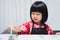 Portrait of Asian child is using a brush dipping pastel green in palette of watercolors placed on table.