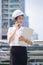 Portrait asian engineering woman standing in wearing white helmet talking telephone and holding paperwork.