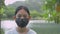 Portrait Asian female teenager wears black face mask looking at camera while standing near the natural pond in the park.