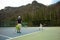 Portrait Asian girl plays tennis with her father and coach at outdoor court with stone mountain and forest background