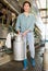 Portrait of a asian woman on a farm, passing by a milking machine, holding a milk flask