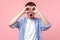 Portrait of astonished curious brown-haired man with small beard and mustache gesturing binoculars. isolated on pink background