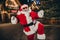 Portrait of astonished excited crazy santa raise fists triumph rejoice newyear evening city center decoration lights