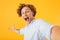 Portrait of astonished happy guy 20s taking selfie photo and screaming, isolated over yellow background