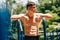 Portrait of athlete young man resting after exercises on horizontal crossbar at sportsground. Handsome muscular shirtless male