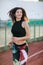 Portrait of Athletic young brunette woman in pink sneakers, leggings and top run on running track stadium at sunset. her hair is