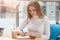 Portrait of attentive ambitious young female sitting at table, writing points in her daily planner, making marks, being satisfied