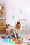 Portrait of attentive little girl sit with young woman teacher explaining how to play with wooden clock in classroom.