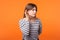 Portrait of attentive nosy young woman with brown hair in long sleeve striped shirt. indoor studio shot isolated on orange