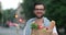 Portrait of attractive adult man holding paper bag with healthy food and standing at street. Crop view of bearded guy in