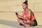 Portrait of an attractive african american athlete sitting on concrete steps with crossed legs and using her smart phone