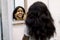 Portrait of attractive African American girl standing near the mirror, applying clay cosmetic mask on her beautiful face