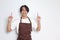 Portrait of attractive Asian barista man in brown apron showing product, pointing at something with hands. Advertising concept.