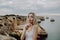 Portrait of attractive blonde woman with silence gesture posing on rocky beach with beauty ocean landscape.