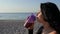 Portrait of an attractive brunette girl drinking a protein shake from a sports bottle on the background of the sea at sunrise.