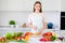 Portrait of attractive cheerful girl cutting tomato cooking fresh meal organic bio product at home light white kitchen