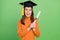 Portrait of attractive cheerful girl wearing master's hat holding scroll paper bachelor degree isolated over green color